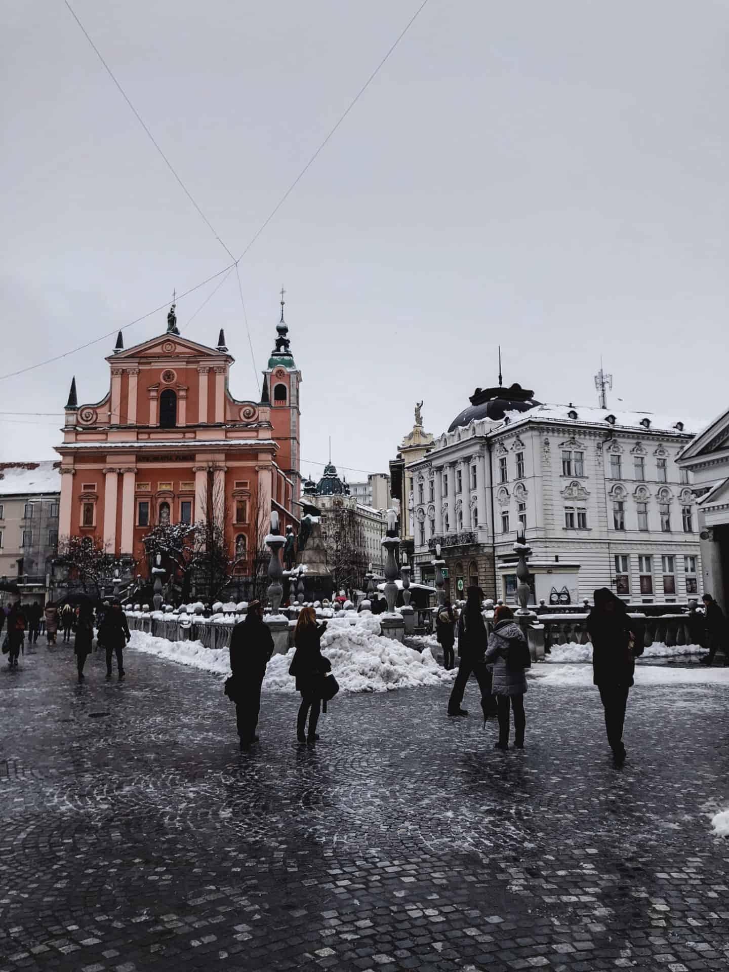 people walking by famous red church in Ljubljana city center during winter