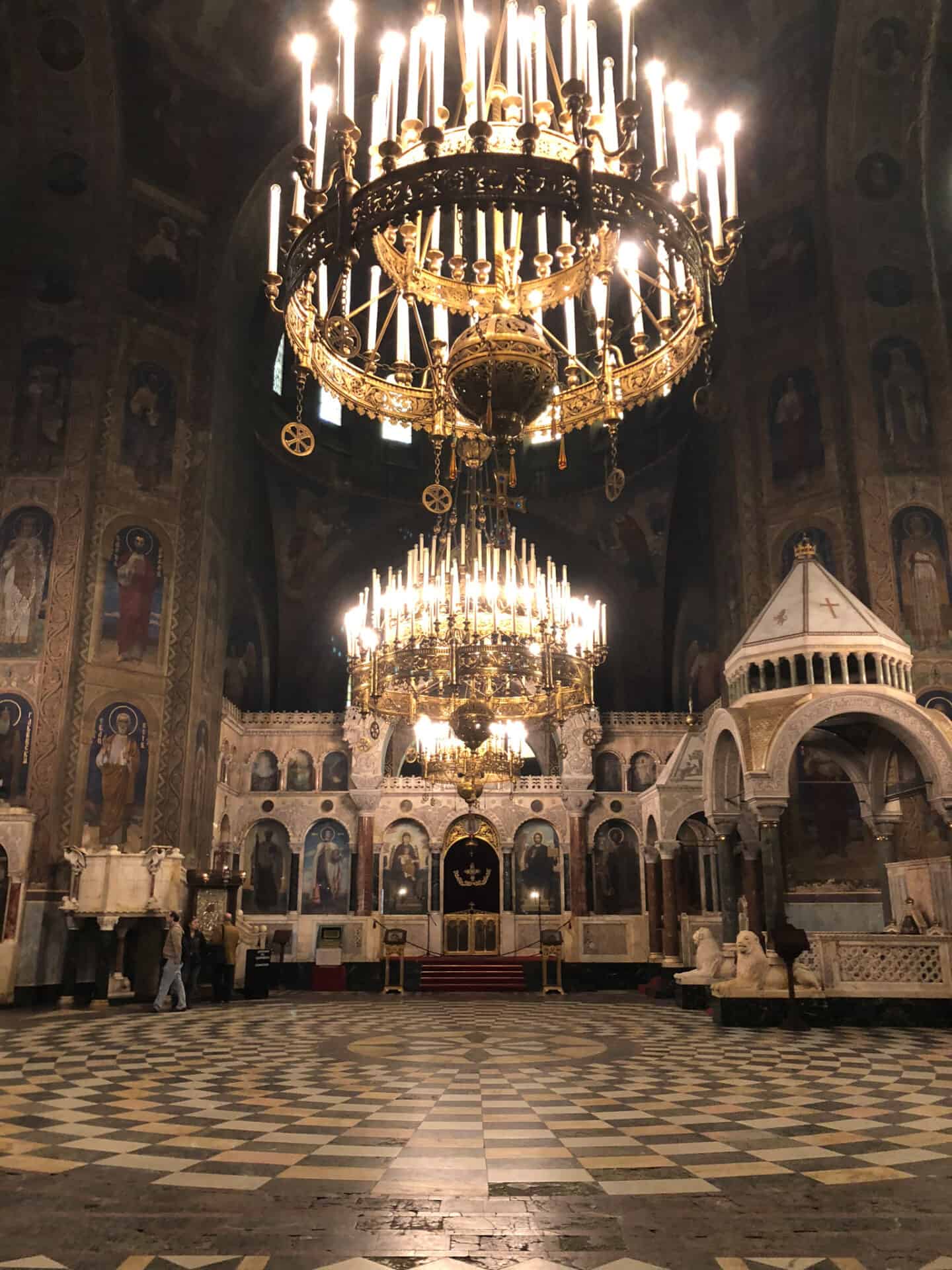 massive lit chandelier in a dark orthodox church and checkered floor