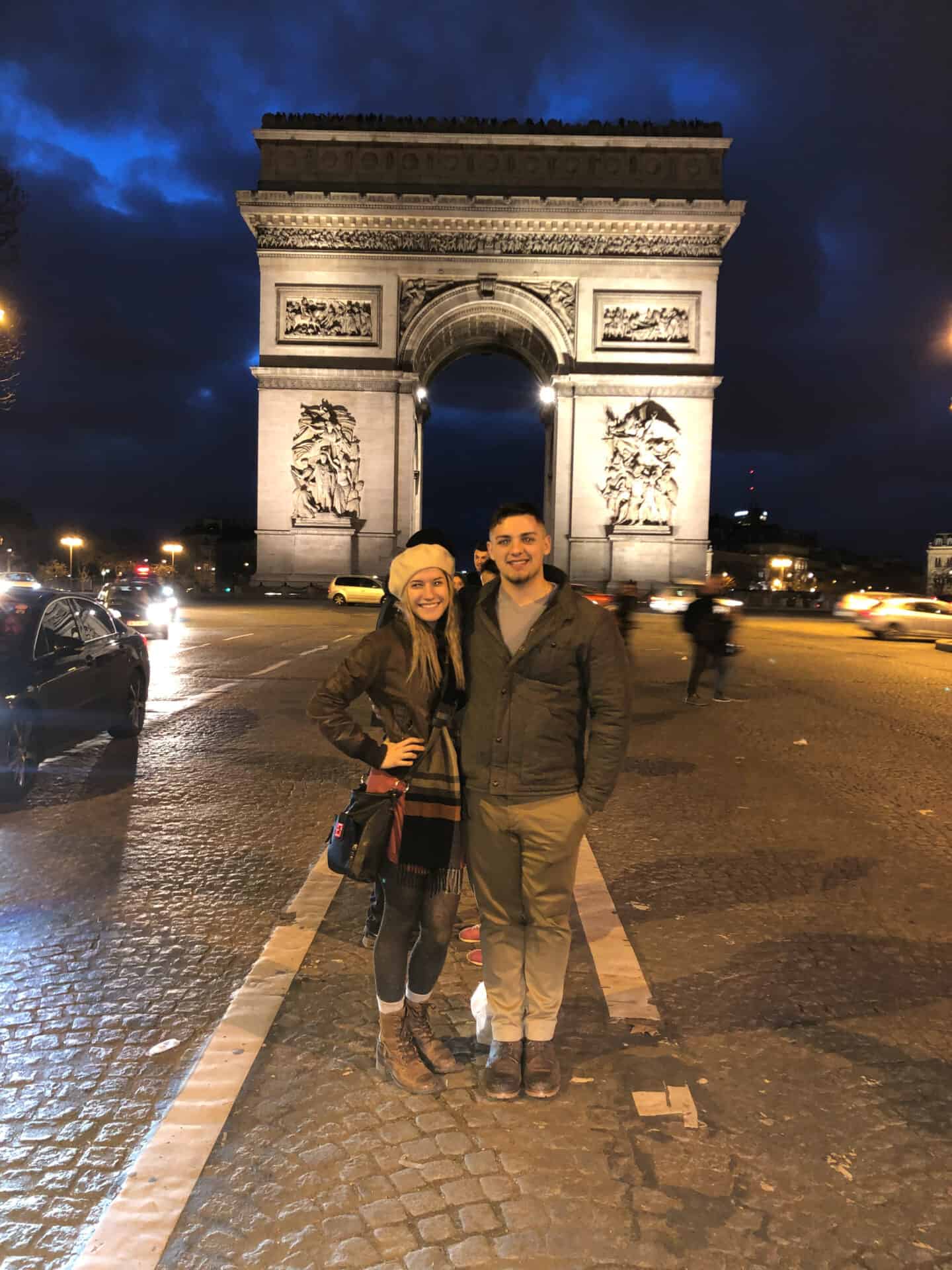 Couple standing at the Arc de Triomphe at night in Paris