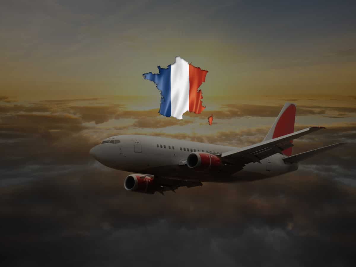 white airplane with French flag flying over a sunset