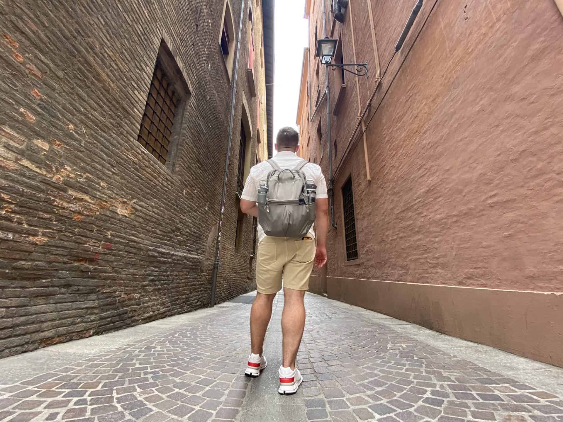 man standing in the middle of the street wearing a grey backpack and facing away from the camera