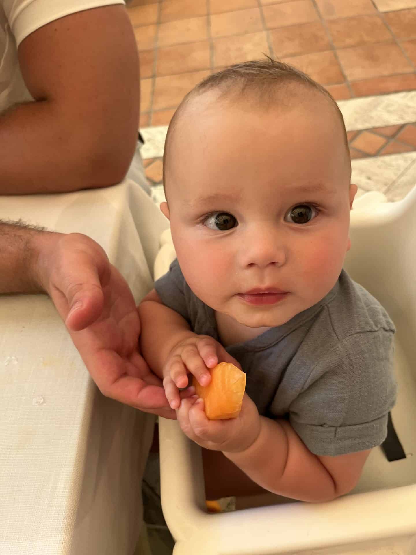 six month old baby in a highchair eating a melon