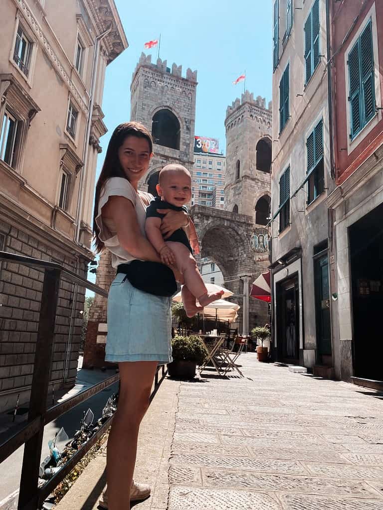 mother holding her six month old babt in front of a castle gate in genoa