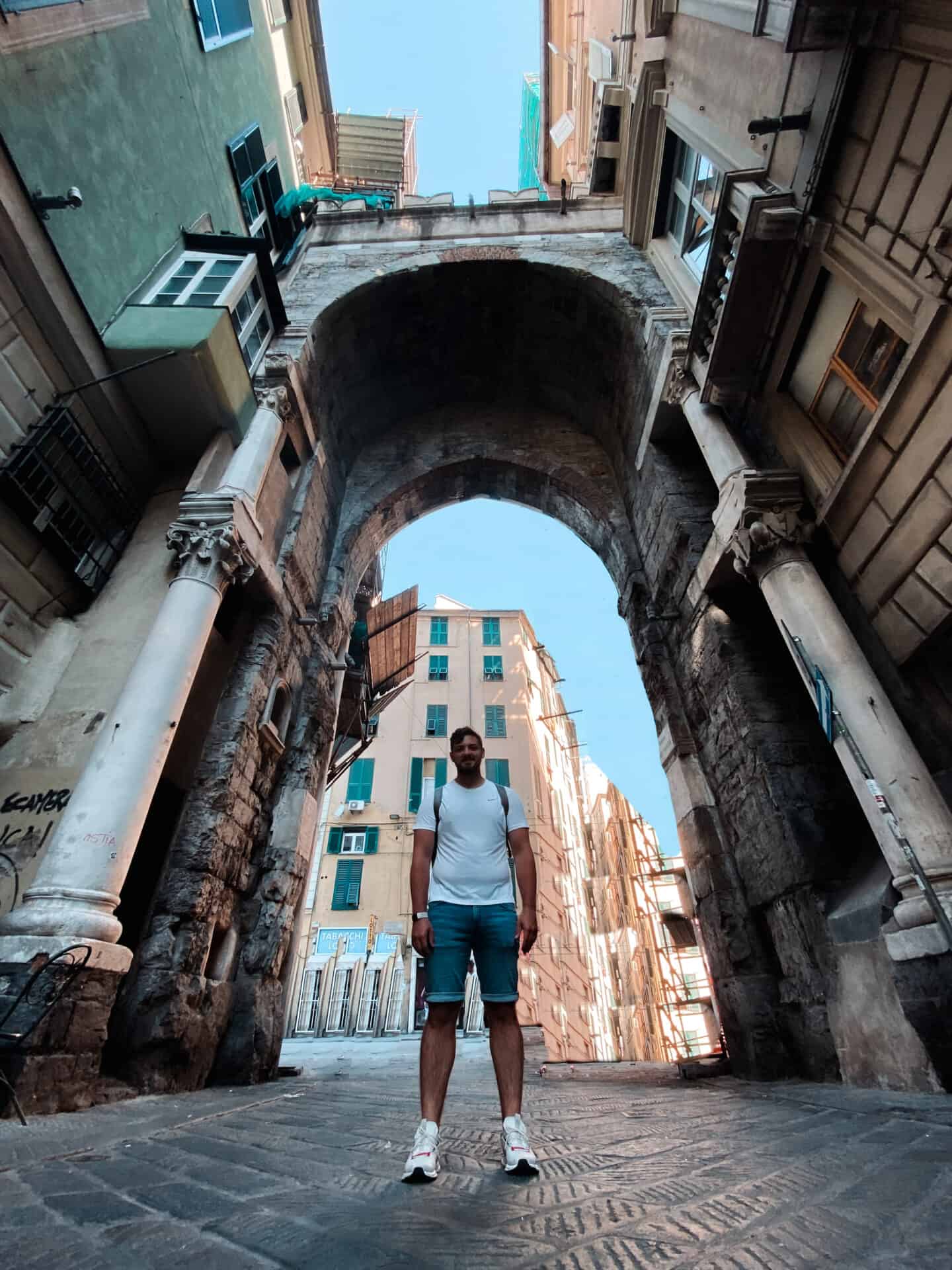 Man standing in the middle of a tall roman archway gate in Genoa