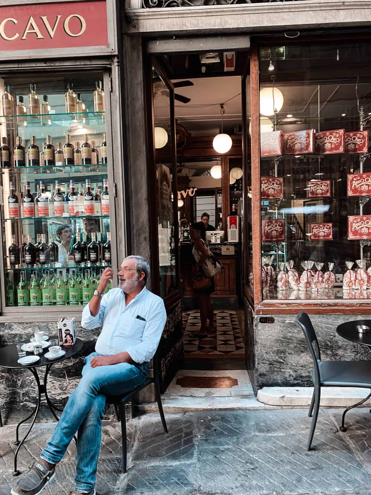 Italian man with a grey beard enjoying a smoke outside of a cafe in Genoa