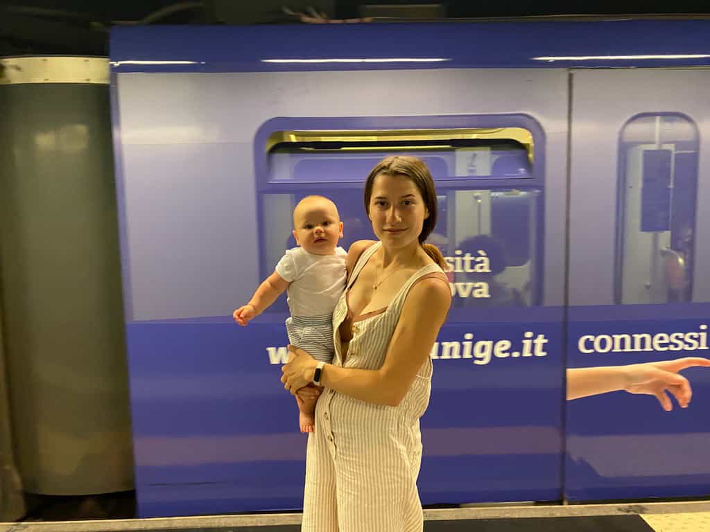 Woman holding six month old son in front of purple metro train in Genoa Italy