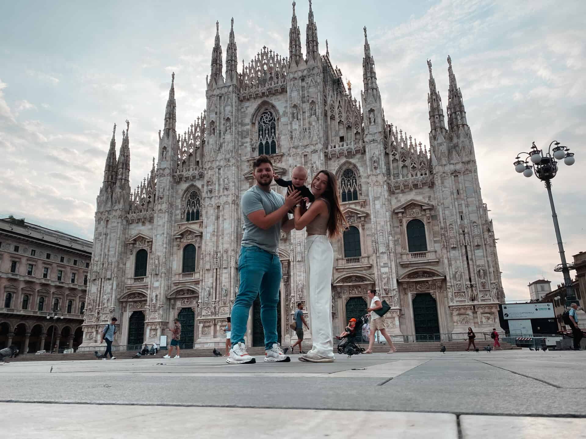 mother and father holding their baby son in the air in front of milano duomo