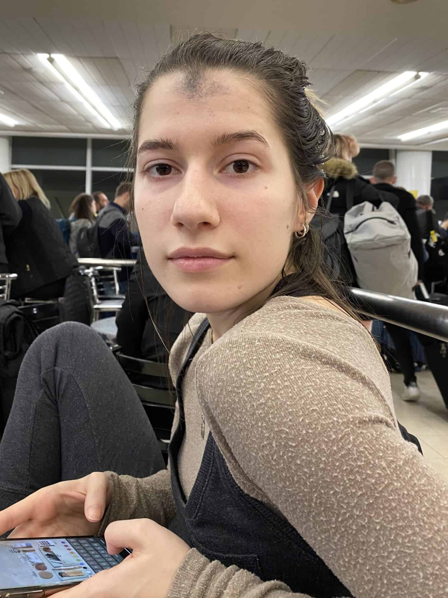 young woman in an airport with religious ashes on forehead