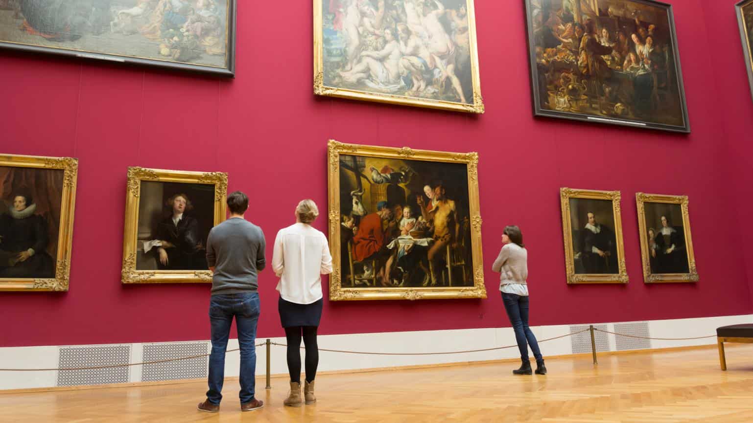 three museum guests looking at paintings on the wall
