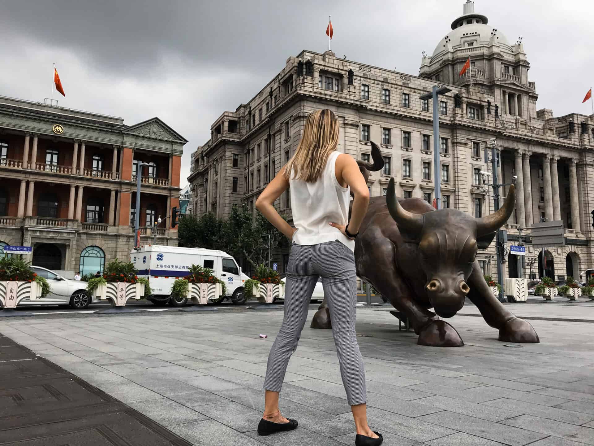 blonde woman standing in front of bull statue in shanghai