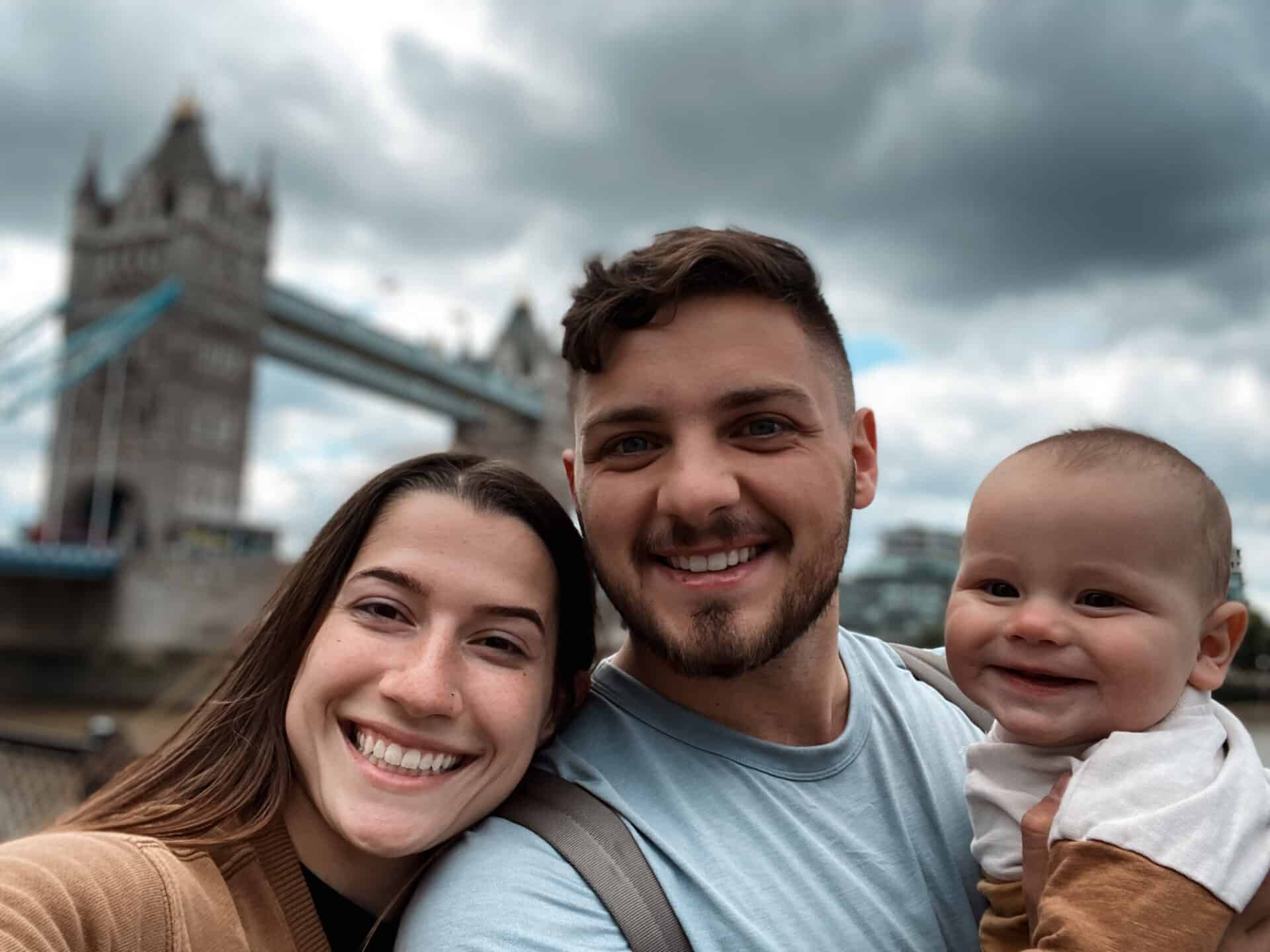 adorbale selfie of young mother, father, and baby in front of London Tower Bridge