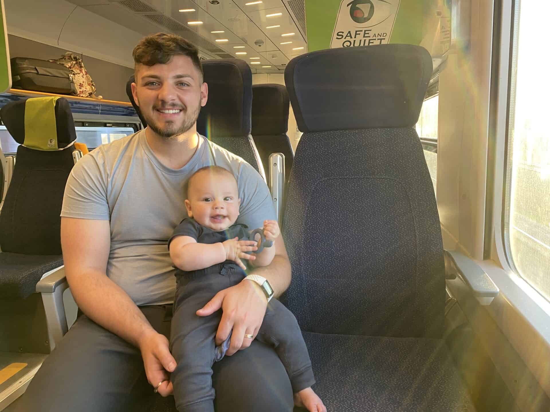 Baby boy sitting on his fathers lap in a train seat