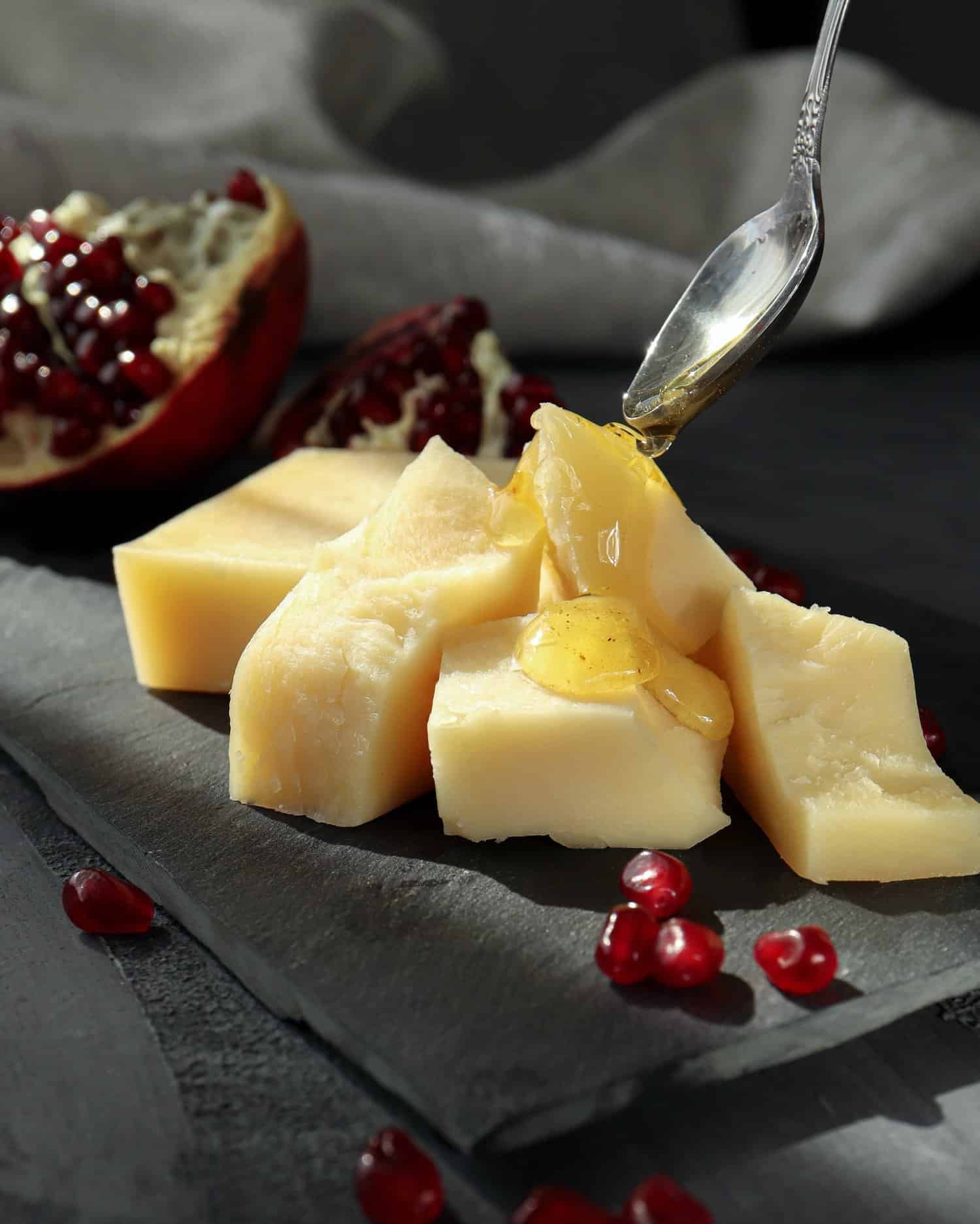 Parmigiano Reggiano cheese with honey and pomegranate seeds on a black plate