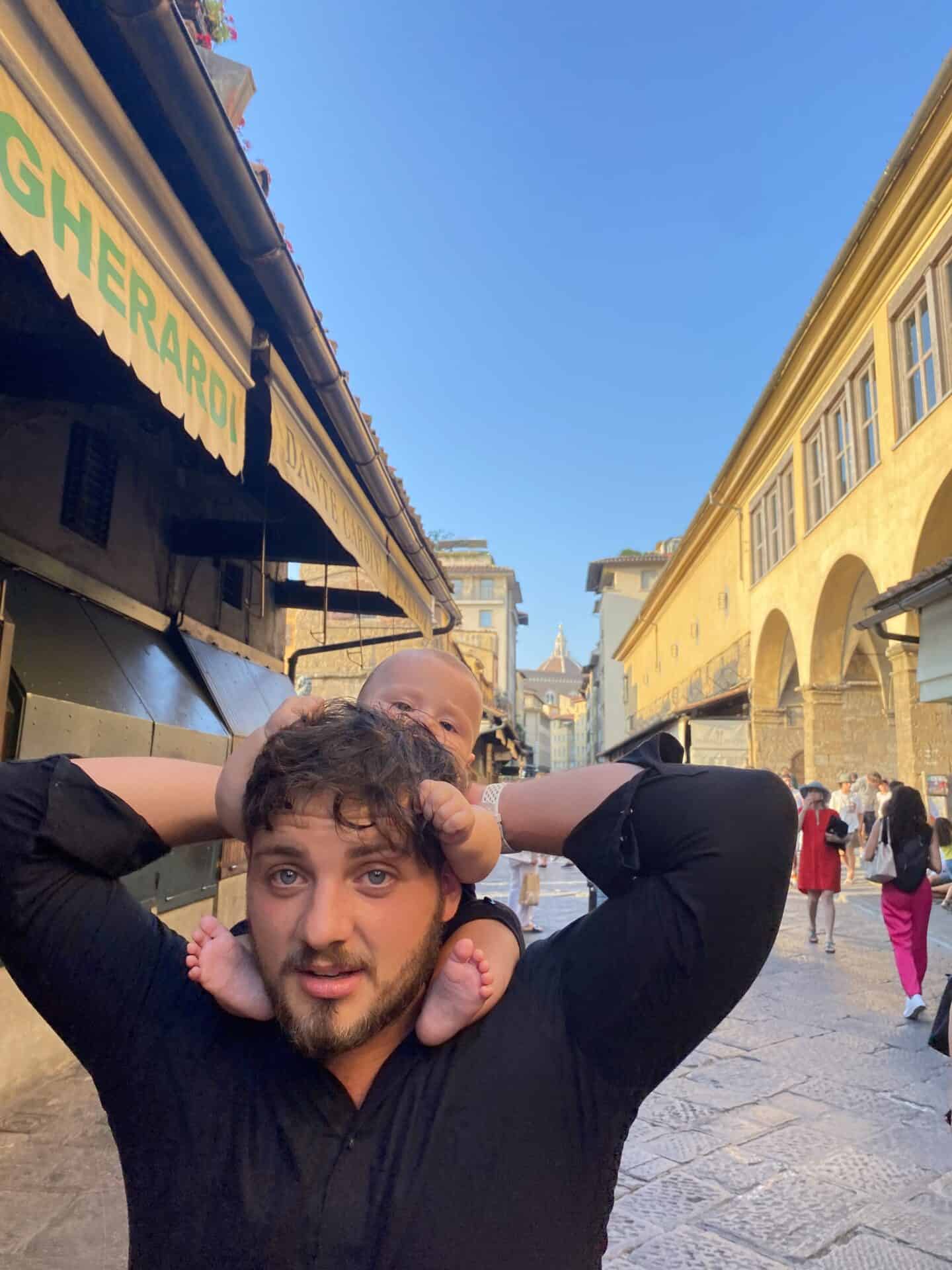 small baby boy sitting on dads strollers as they walk through the streets of florence