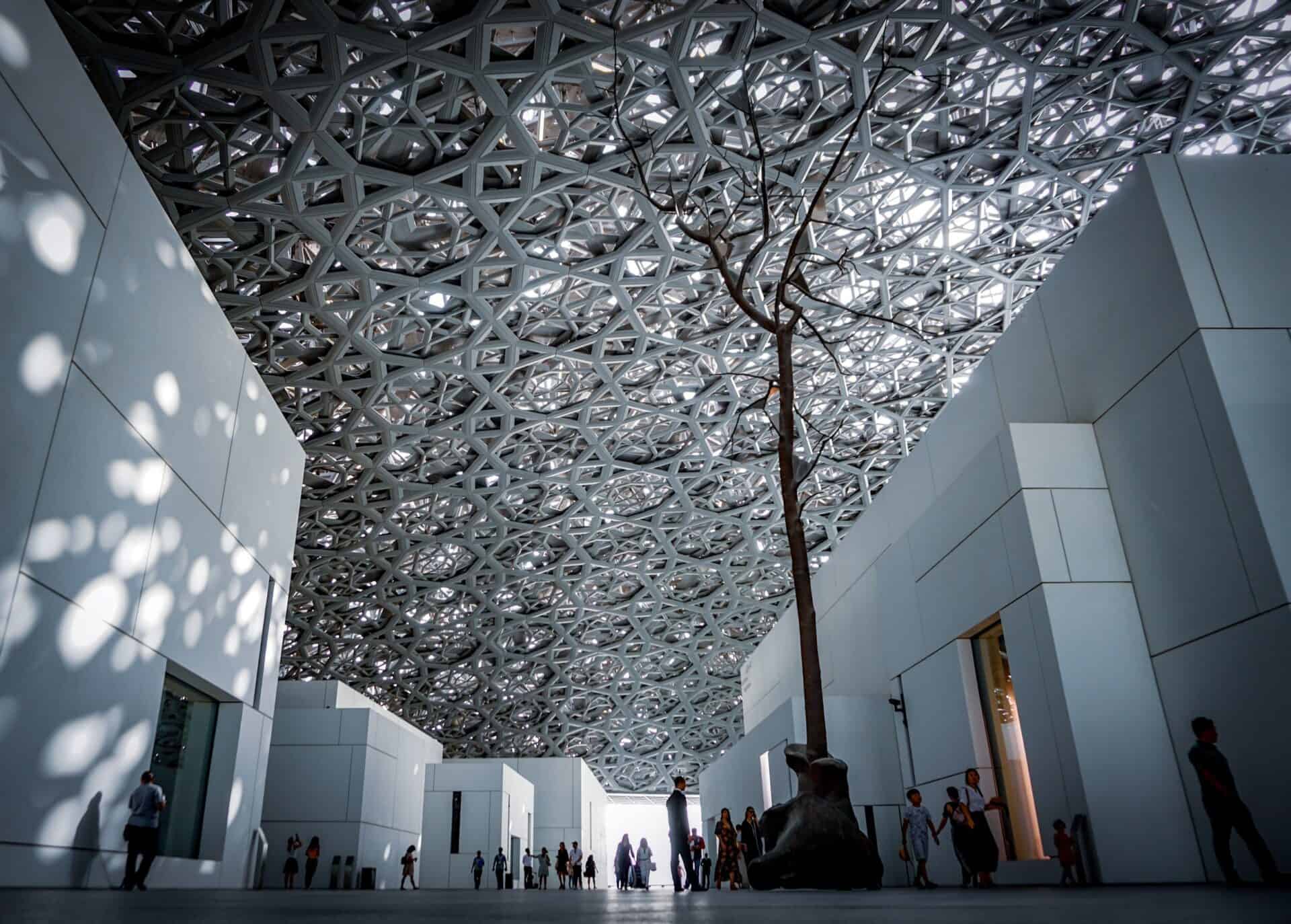 People walking in the Abu Dhabi Louvre Museum with black and white tree art
