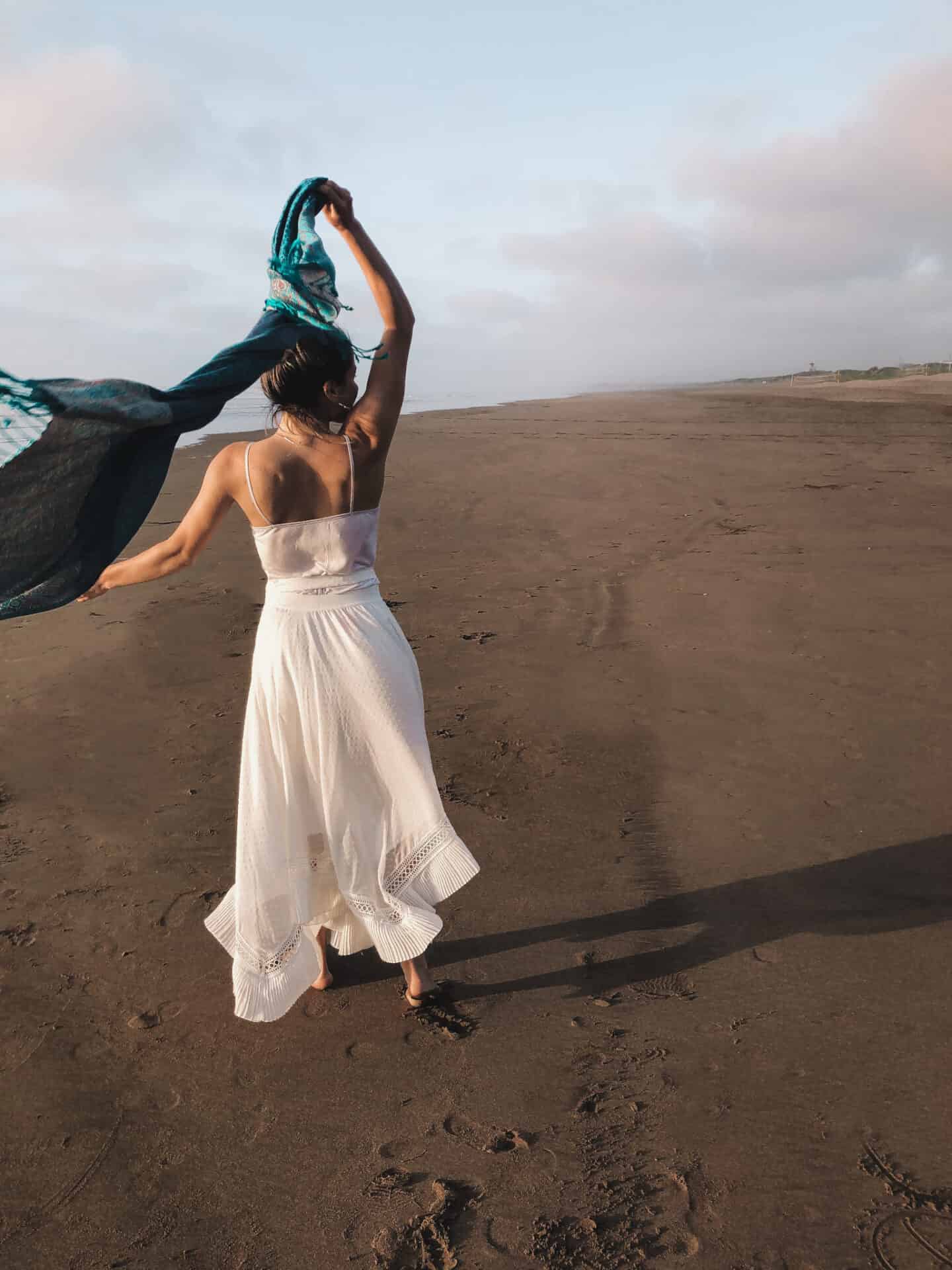 female model in white dress and blue scarf dancing on a beach in el jadid