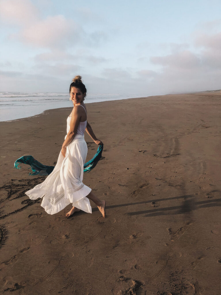 female model in white dress and blue scarf dancing on a beach in el jadid
