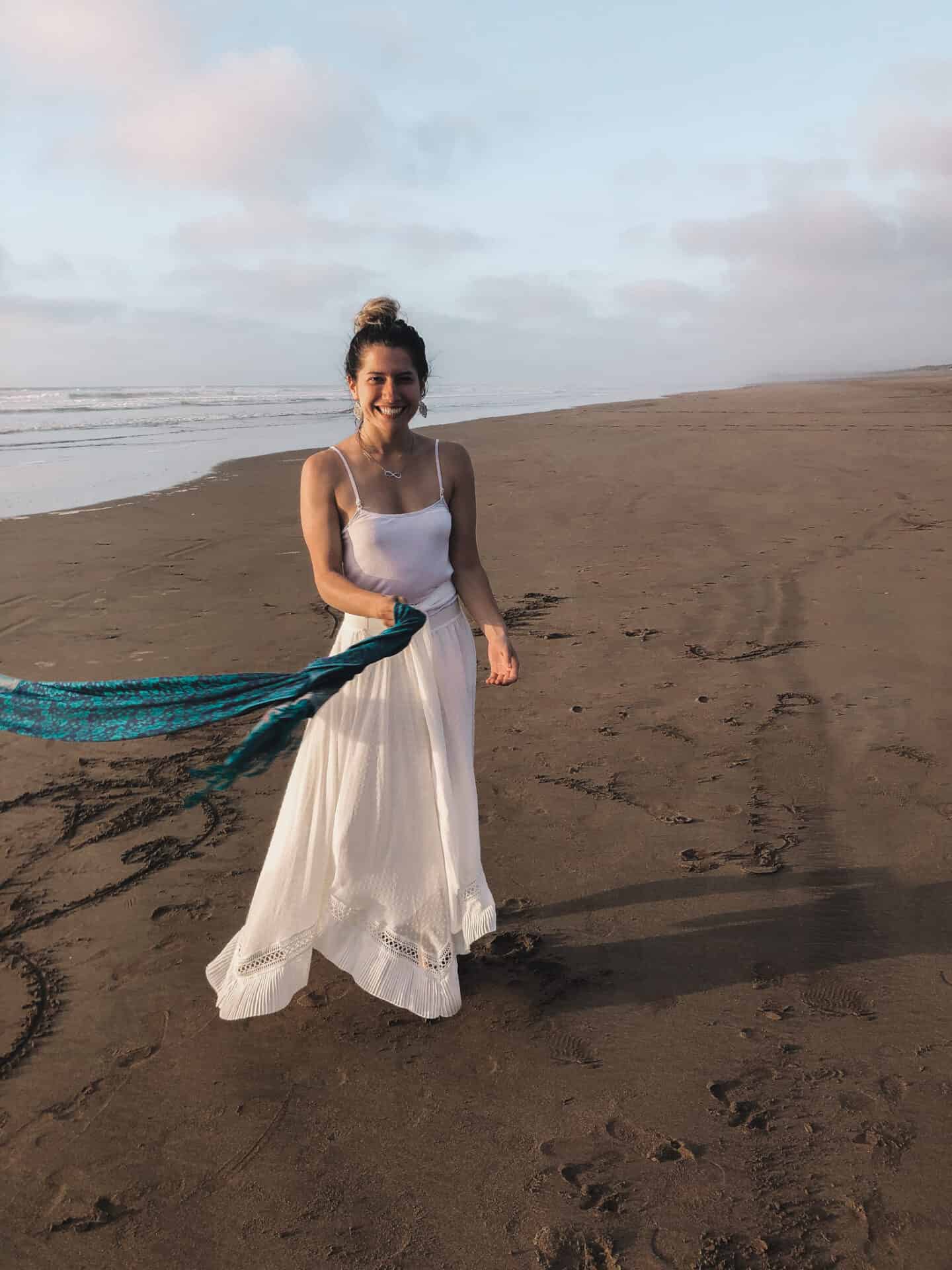 female model in white dress and blue scarf laughing on a beach in el jadid