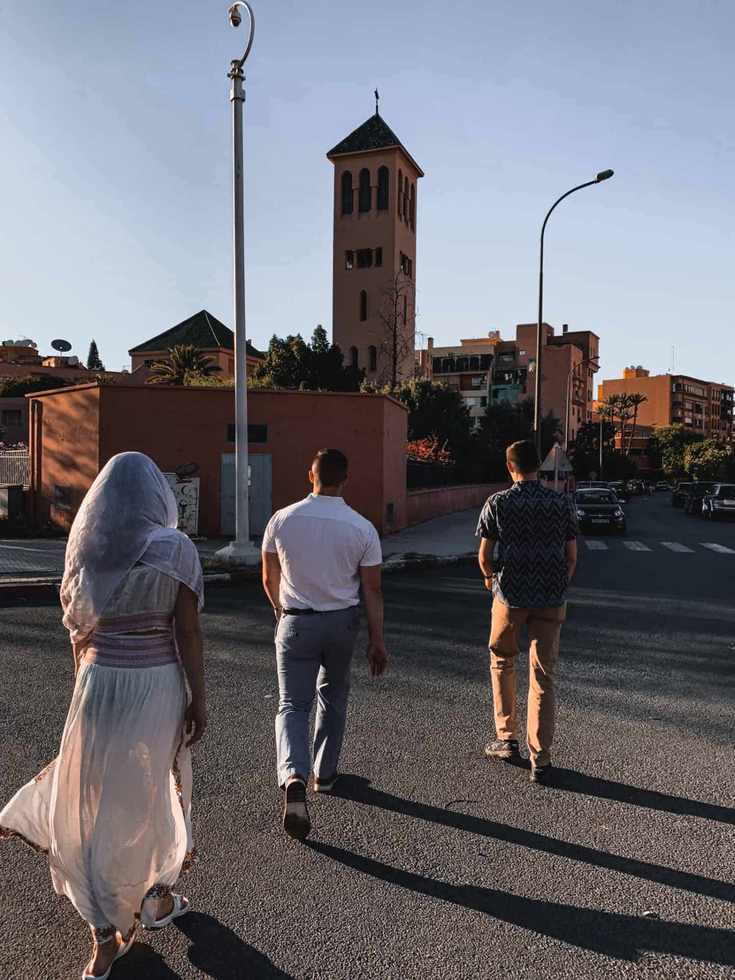 three persons walking by a minaret in marrakech at sunset