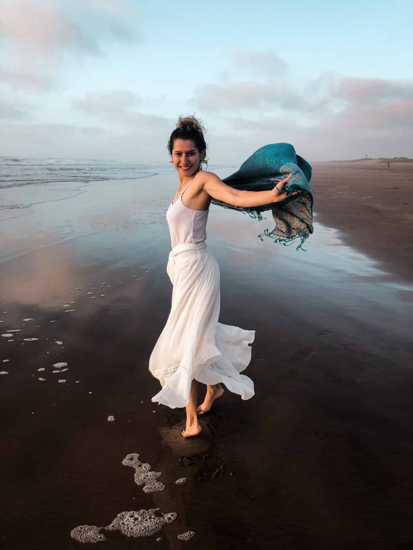 female model in white dress and blue scarf laughing on a beach in el jadid