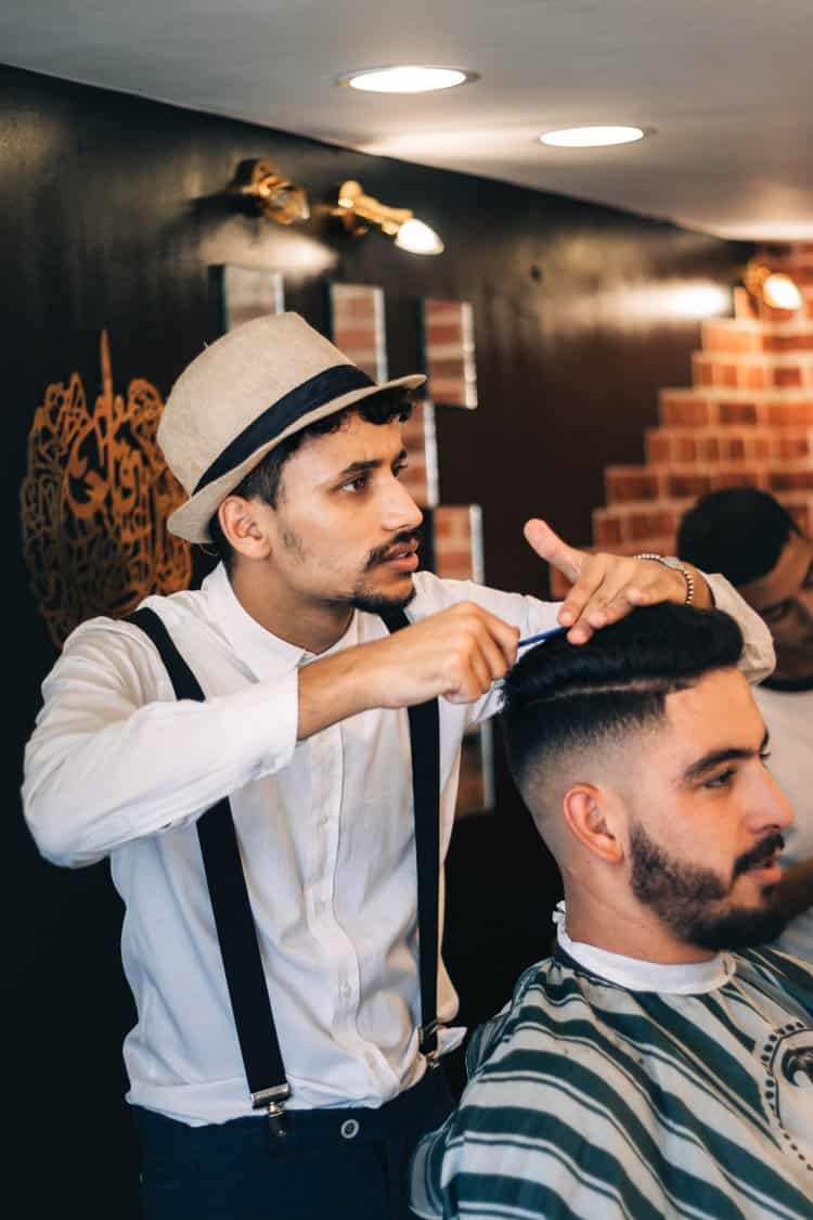 Italian barber with fedora cutting man's hair in Rome