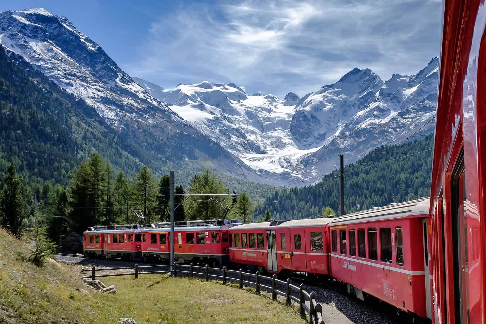 red and white Bernina Express train near green field viewing mountain and green trees in The Swiss Alps