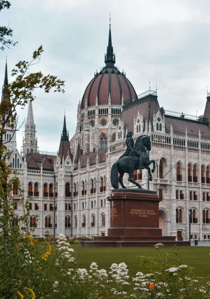 black statue in front of white concrete parliament building in Budapest with terracotta roof during daytime