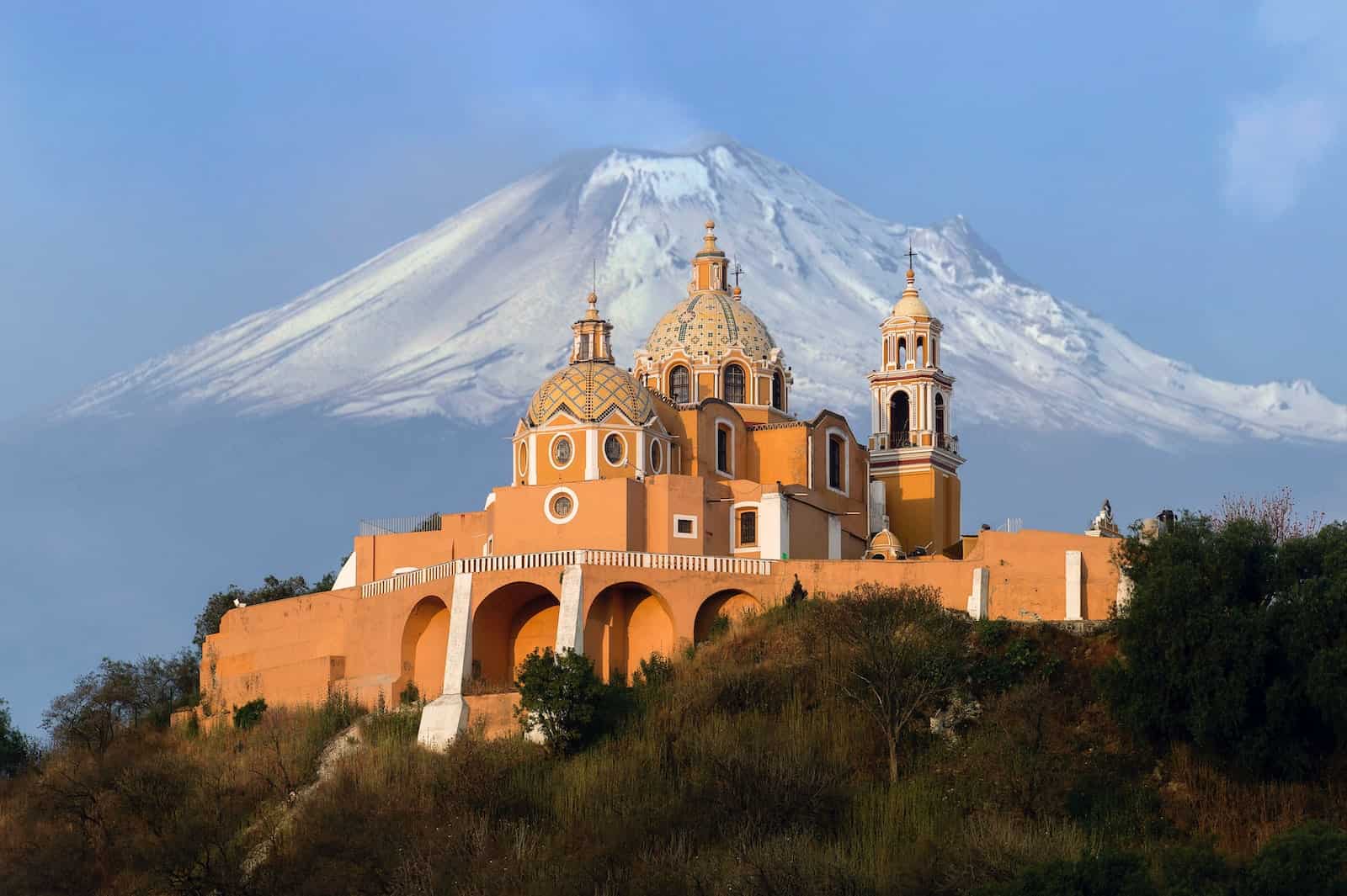 aerial photography of orange cathedral in cholula mexico with volcano in background