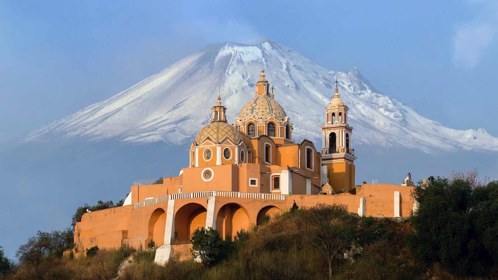 aerial photography of orange cathedral in cholula mexico with volcano in background
