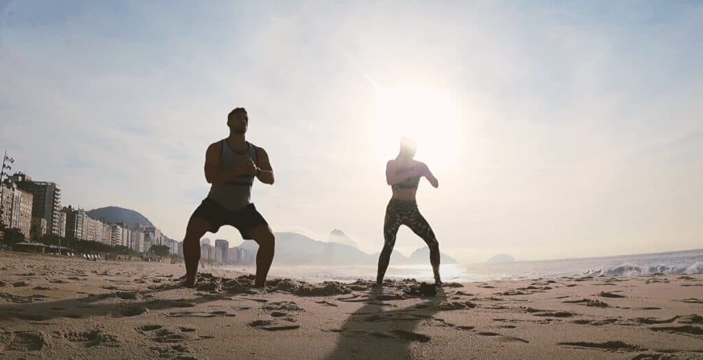 silhouette of couple completing air squats on copacabana beach during sunrise