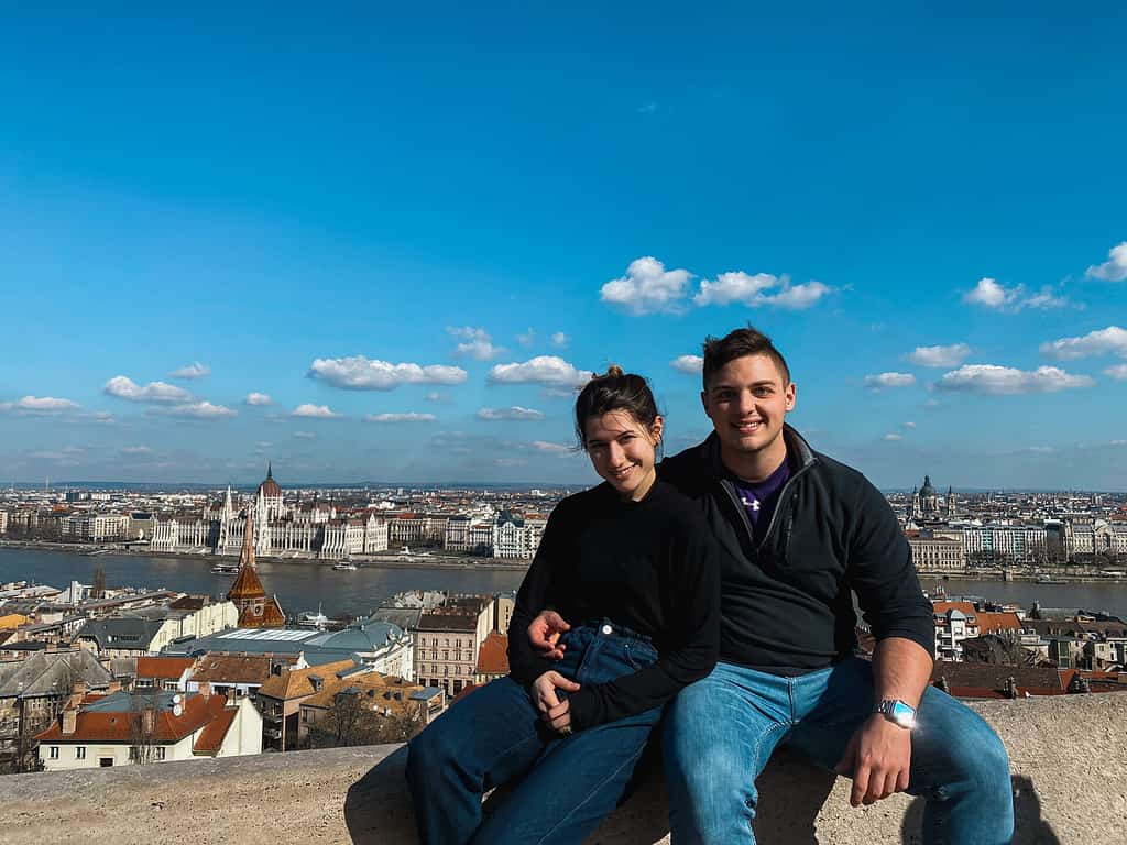 couple in black shirts and blue jeans embracing on budapest hill lookout