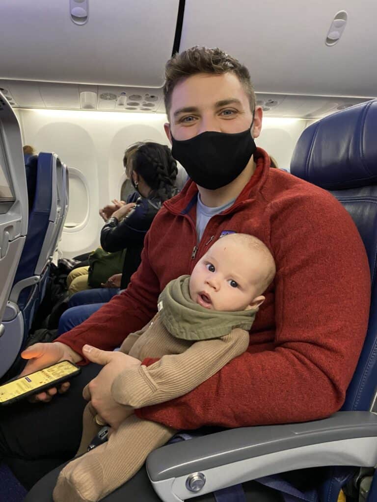 two month old baby in bandana sitting on fathers lap on an airplane