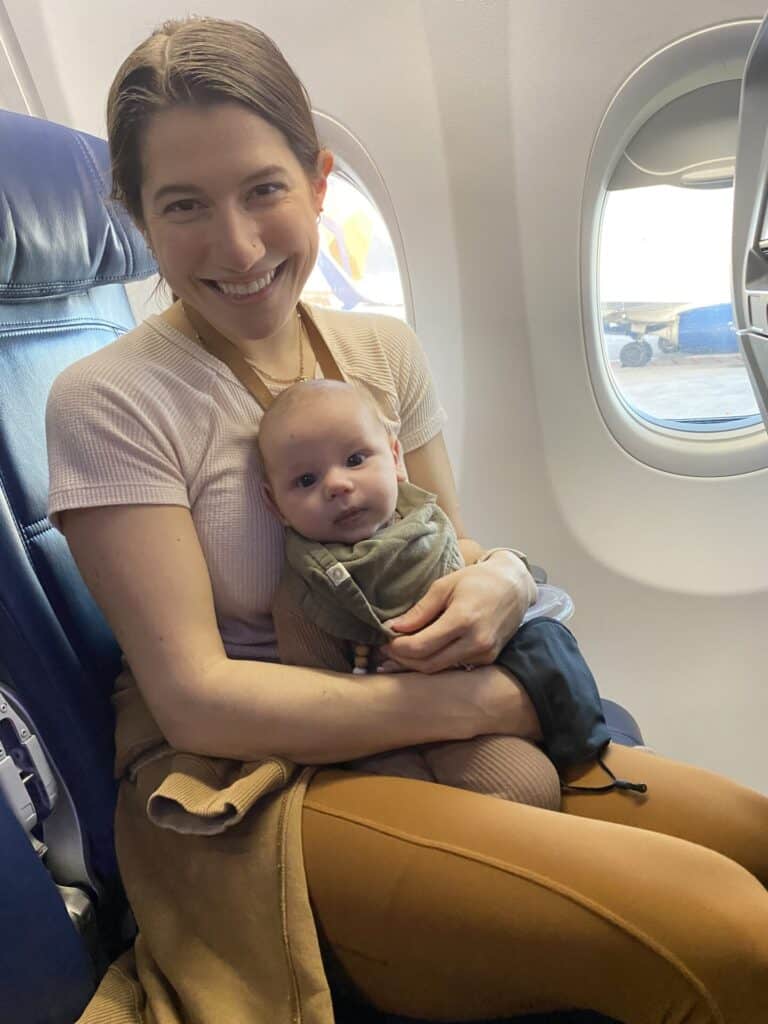 two month old baby in bandana sitting on mothers lap on an airplane