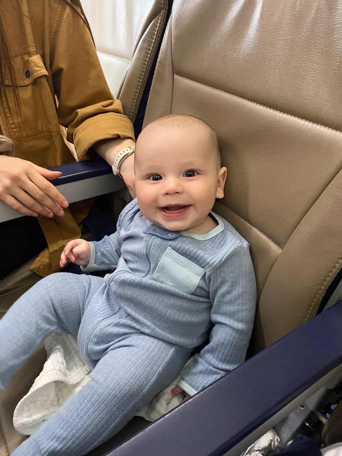 happy 3 month old baby in blue pajamas sitting in airplane seat