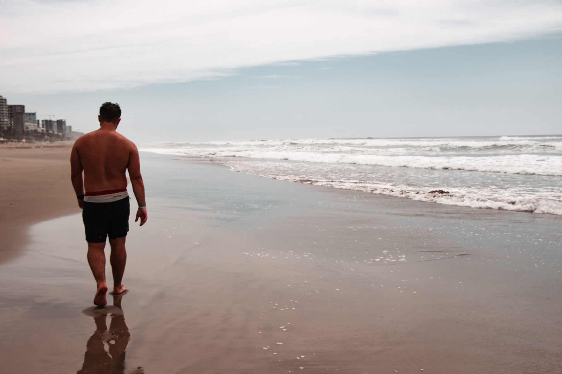 shirtless male walking along grey beach