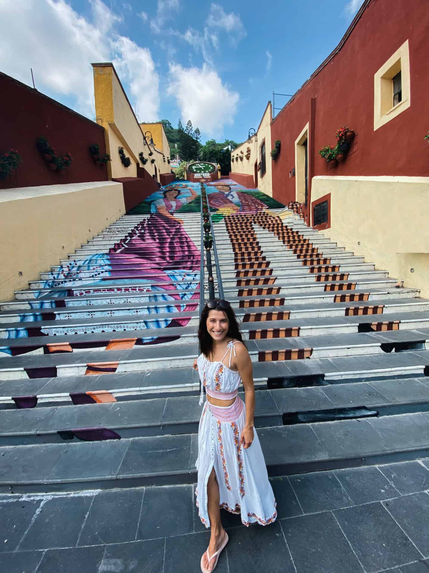 woman in white dress standing in front of iconic atlixco colorful stairs