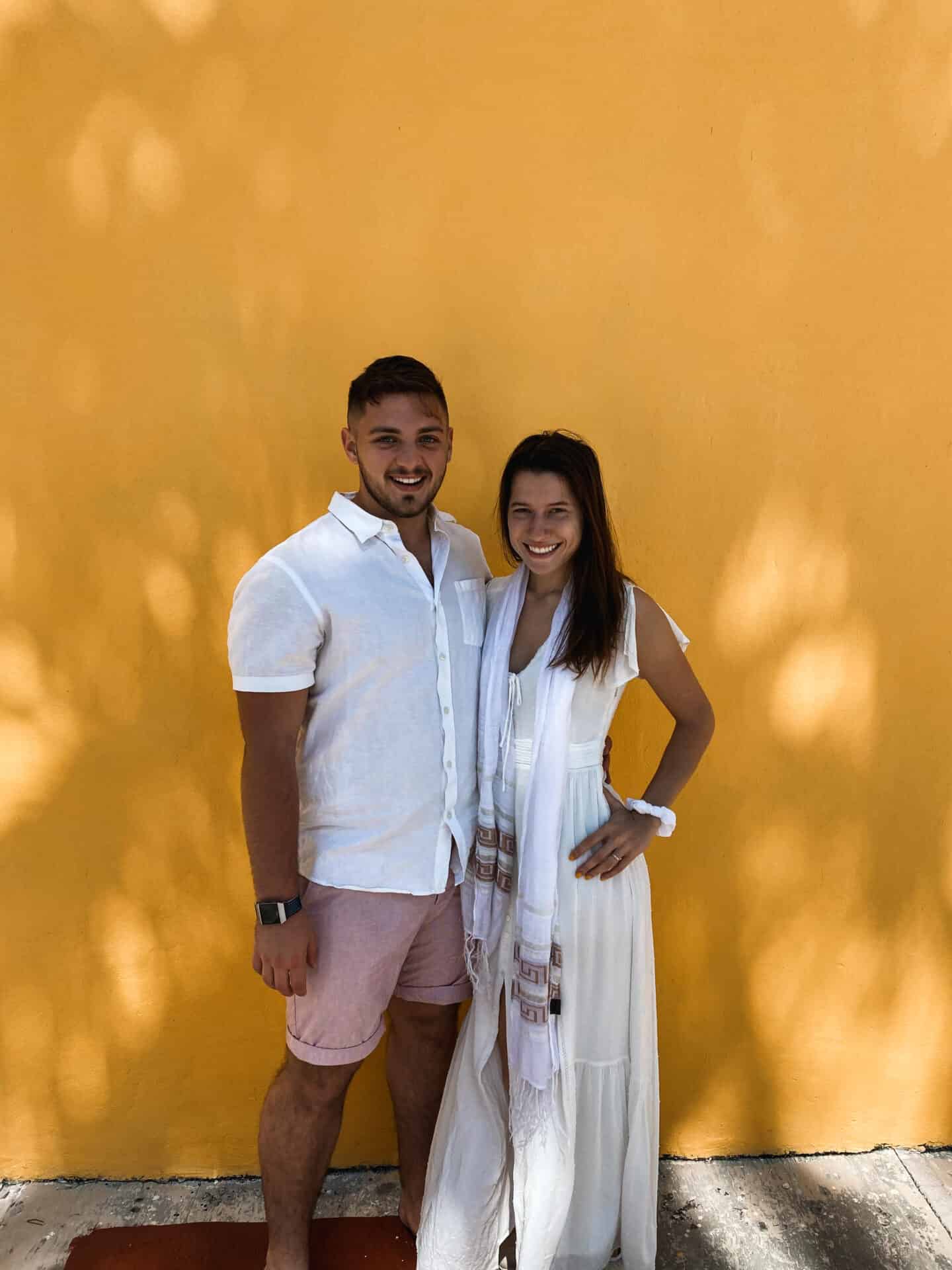couple dressed in white posing in front of mustard yellow mexican wall