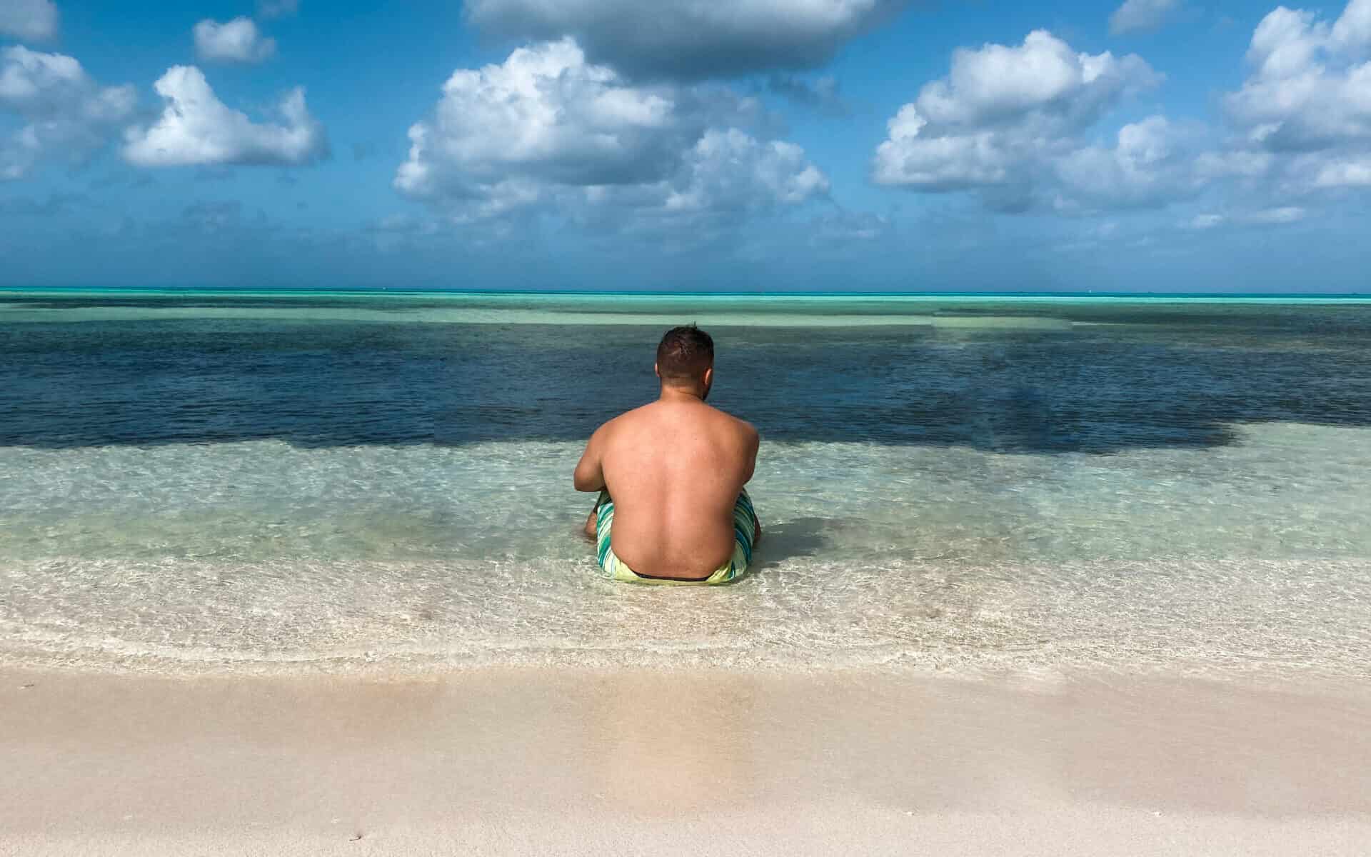 man sitting on crystal clear blue beach in mexico