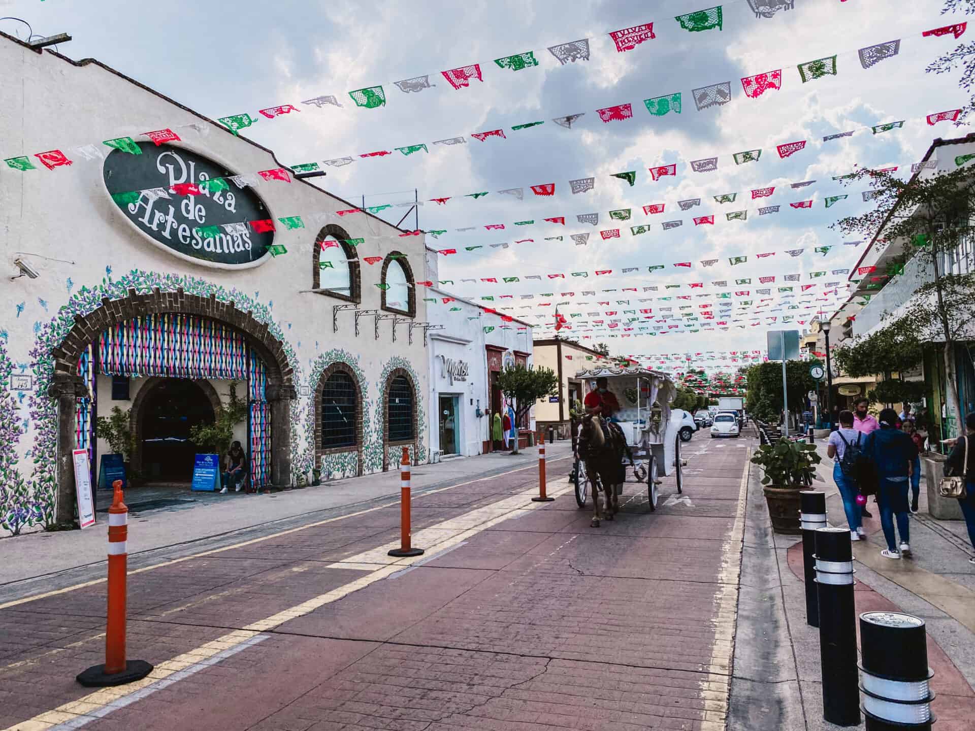 horse drawn carriage underneath red white and green streamers strung accros mexican street
