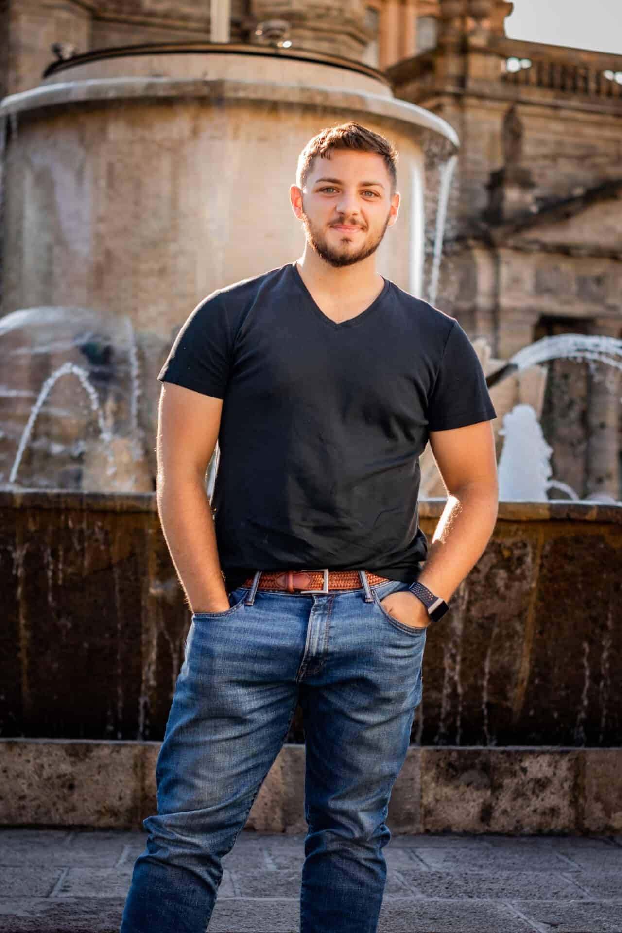 male model in black tshirt and dark blue jeans in front of fountain in center of guadalajara