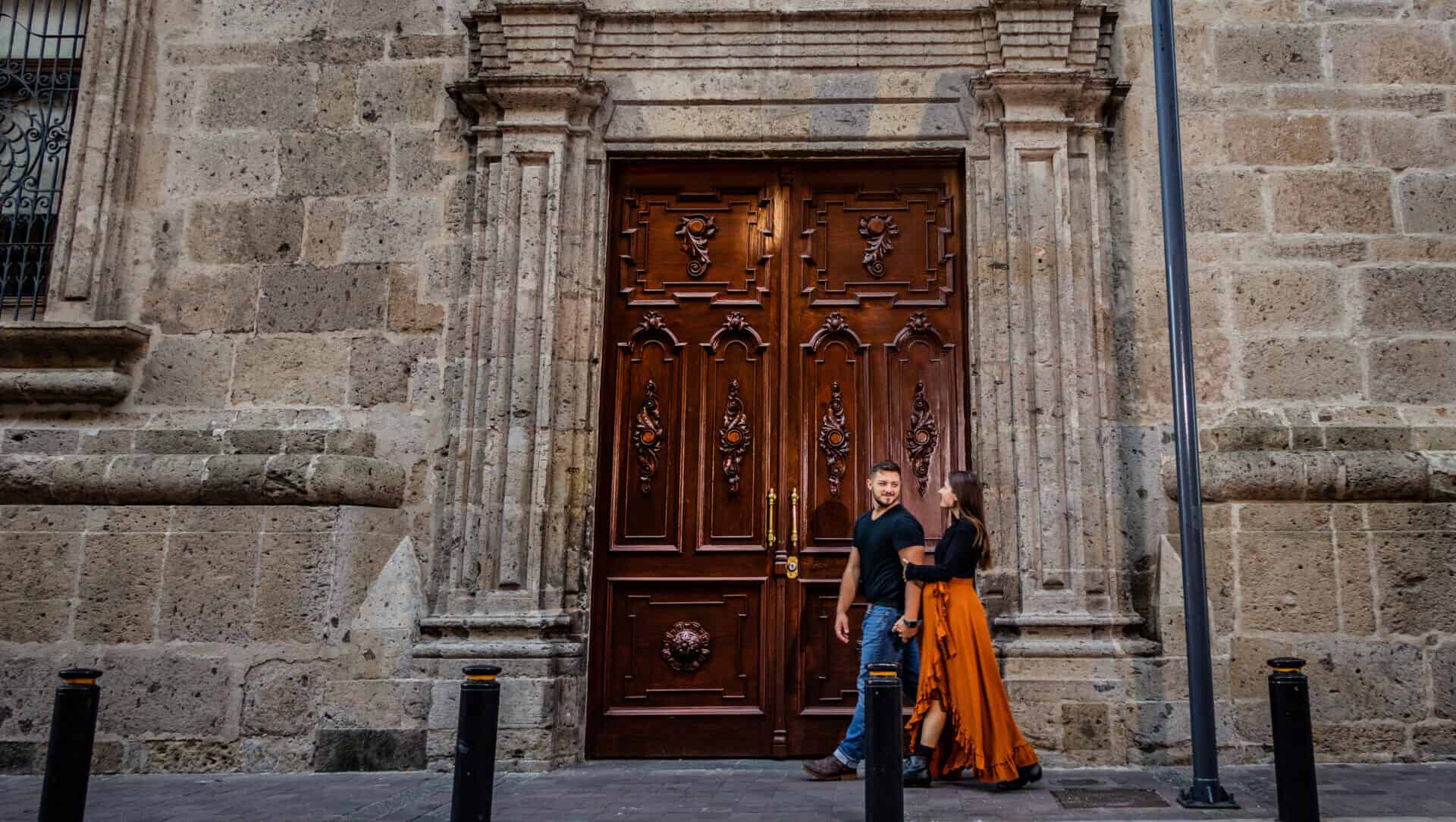 couple in black walking by large brown door