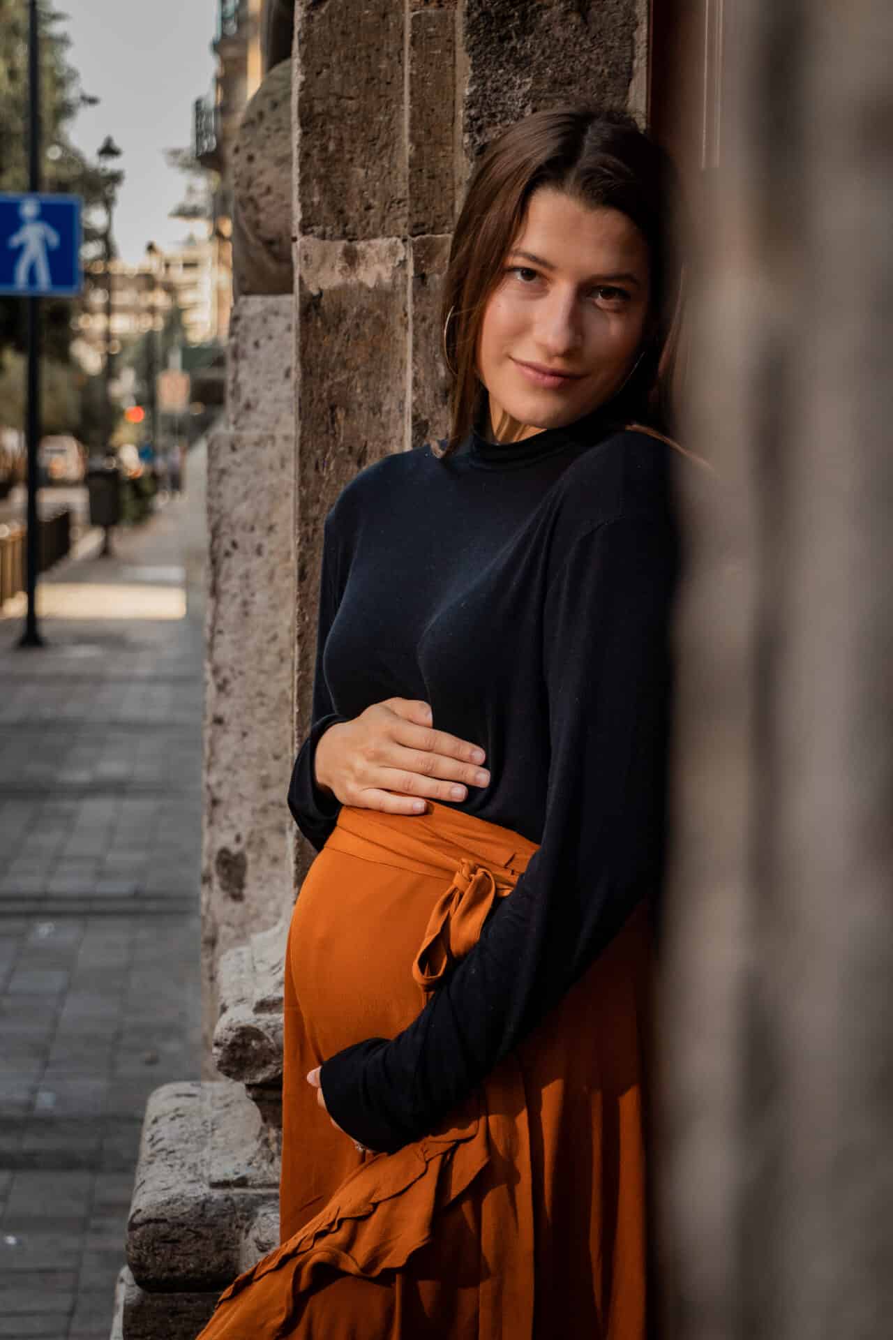 pregnany woman in black shirt and orange skirt holding her belly