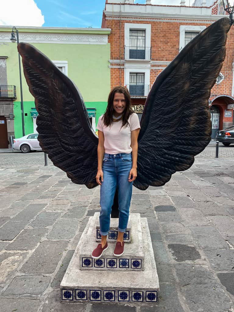 woman in jeans posing under iron angel wing street art