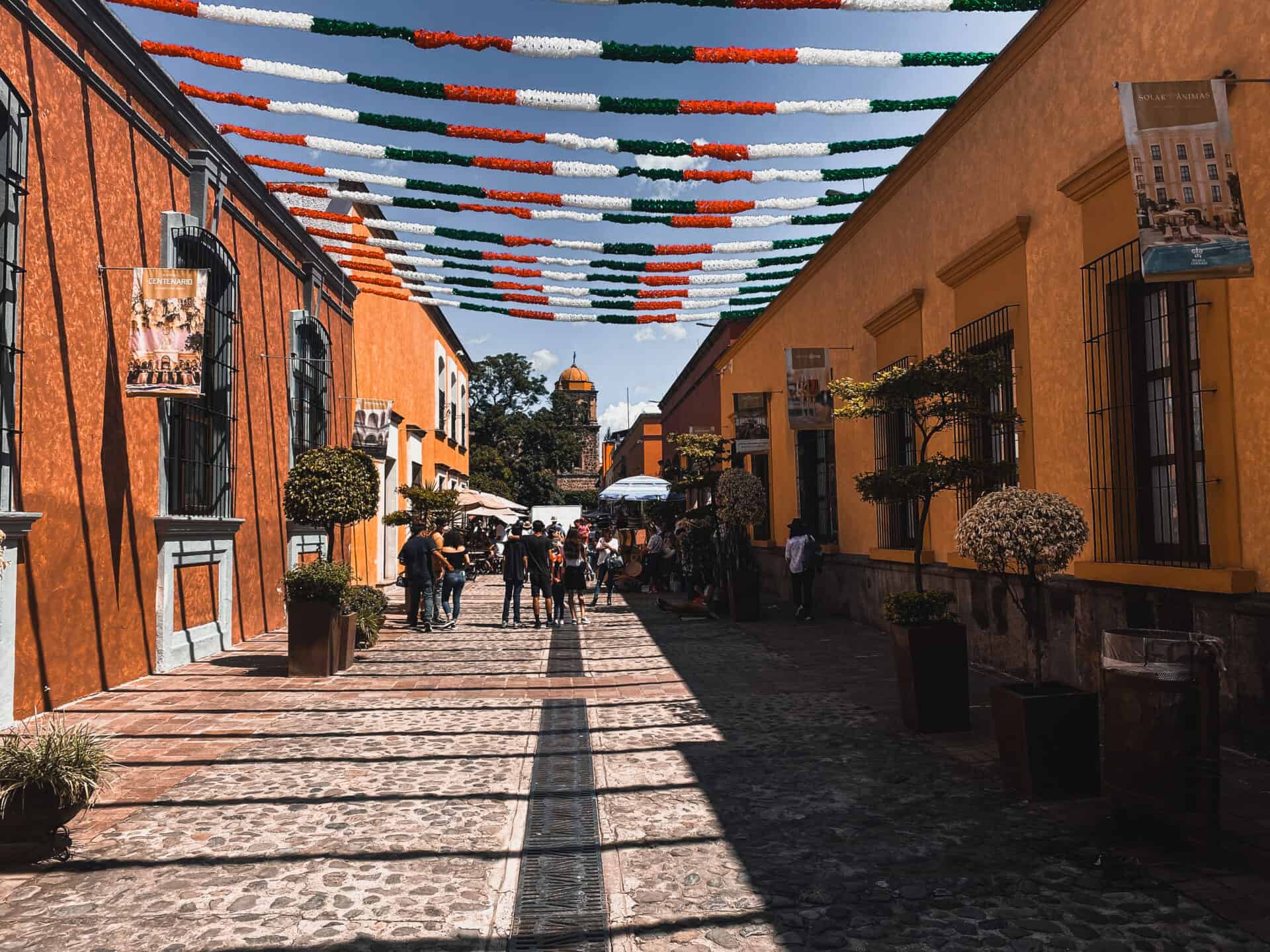 cobblestone mexican street with yellow concrete buildings and red, white and green garlands