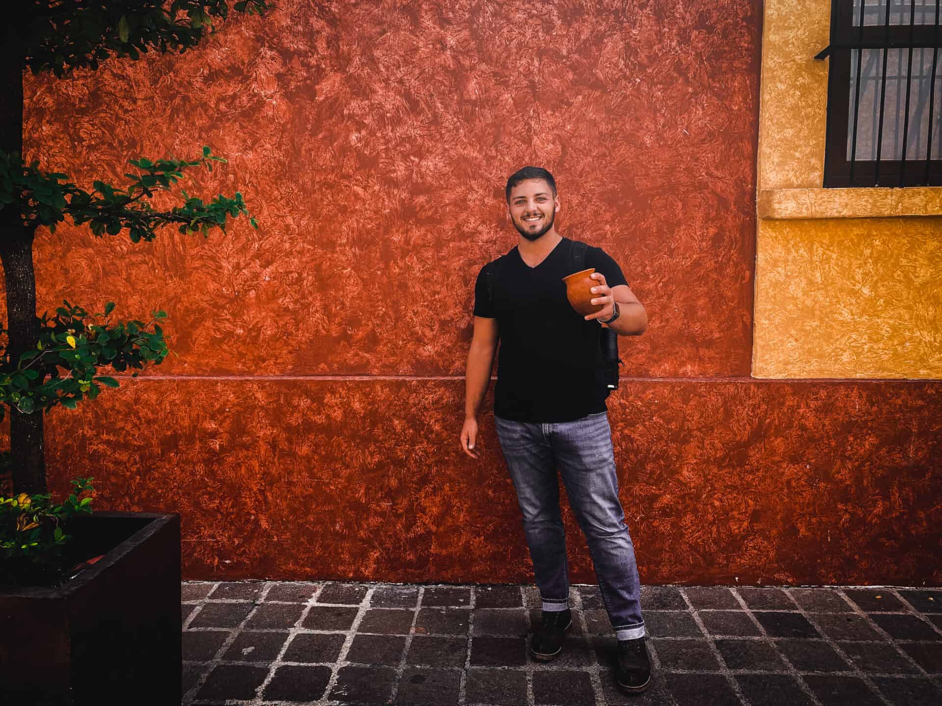 man holding a clay canteen in front of red concrete wall in tequila mexico