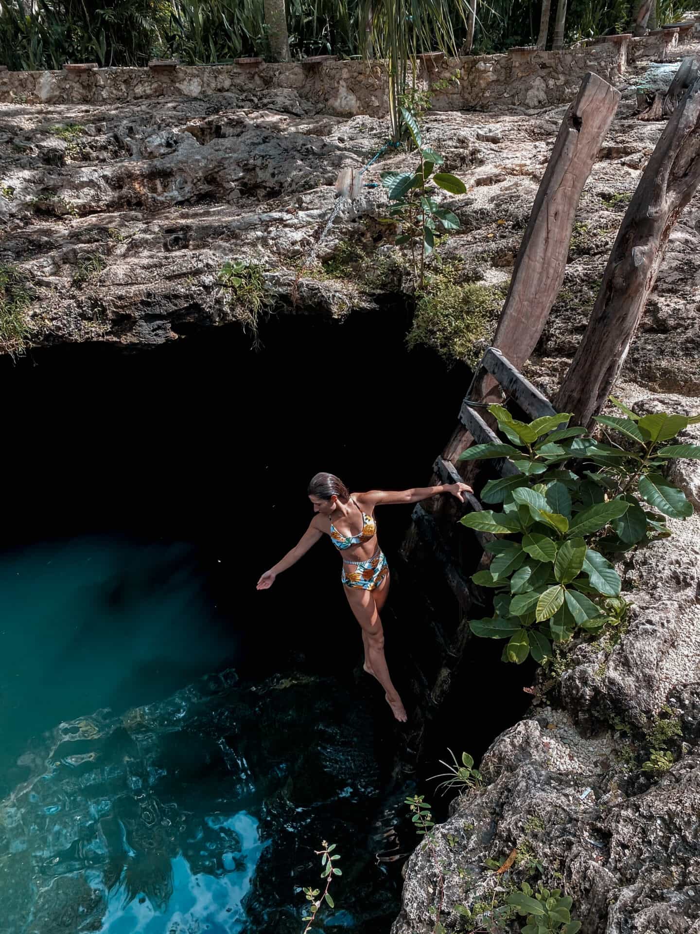 woman dangling from ladder over a blue mexican cenote in Tulum