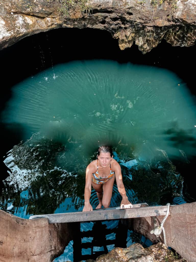 woman on ladder climbing out of dark cenote waters