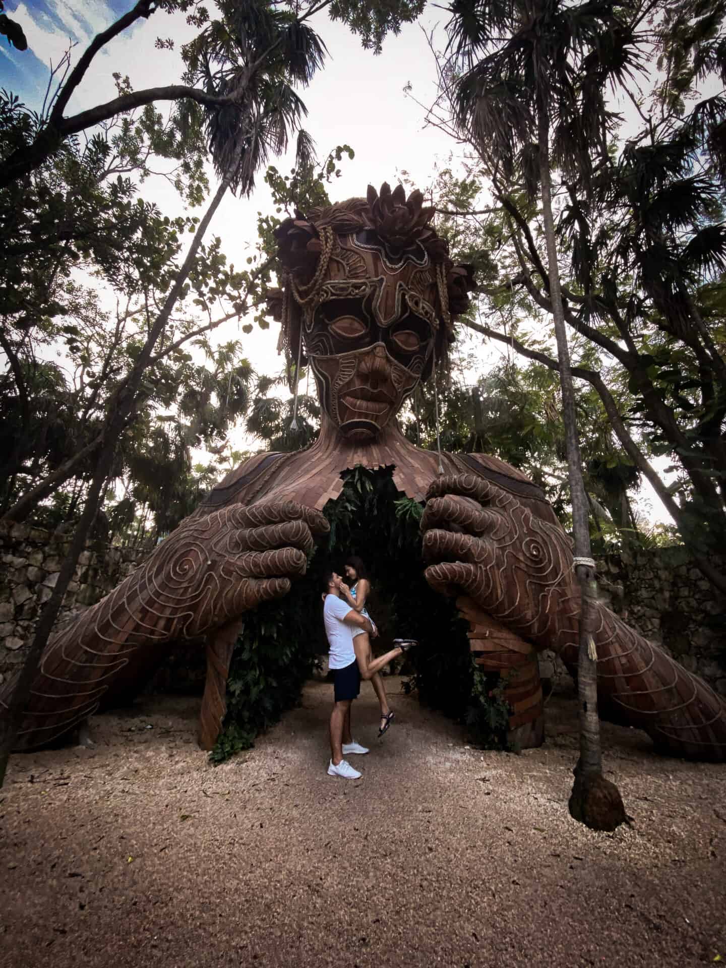 couple embracing underneath massive Ven a la luz open heart sculpture in jungle of Tulum