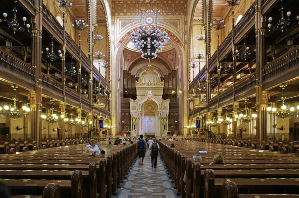 Interior of a grand golden synagogue with long aisle and pews