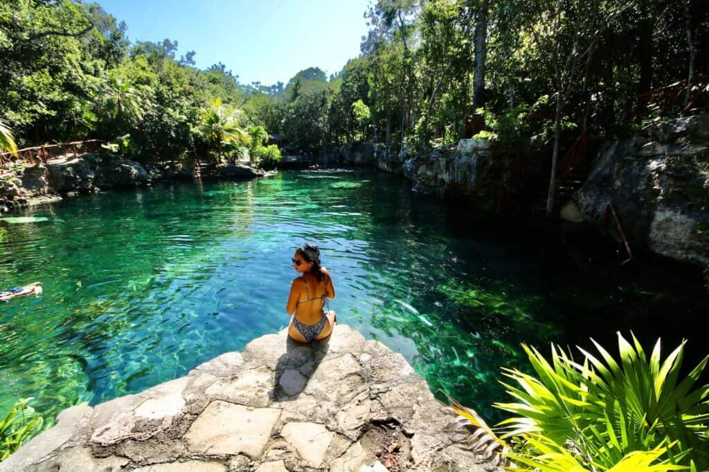 woman sitting on rock overlooking large green body of crystal clear water with jungle around